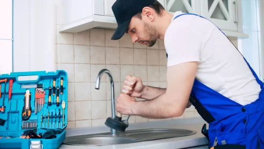 A plumber is using a plunger to unclog a kitchen sink.