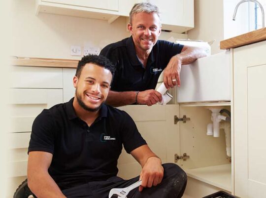 Two plumbers smiling at looking at the camera