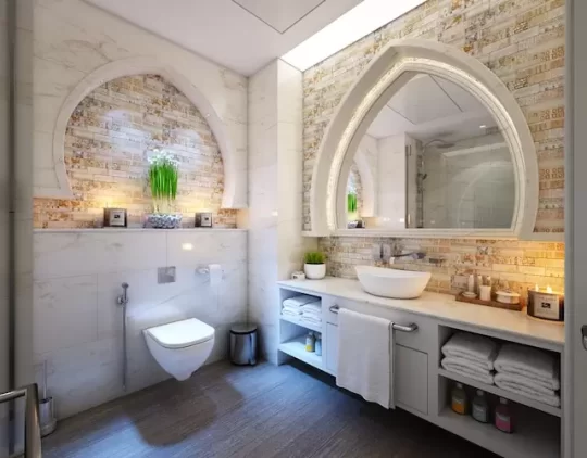 A modern bathroom features marble walls and a large arched mirror above a counter with a white vessel sink